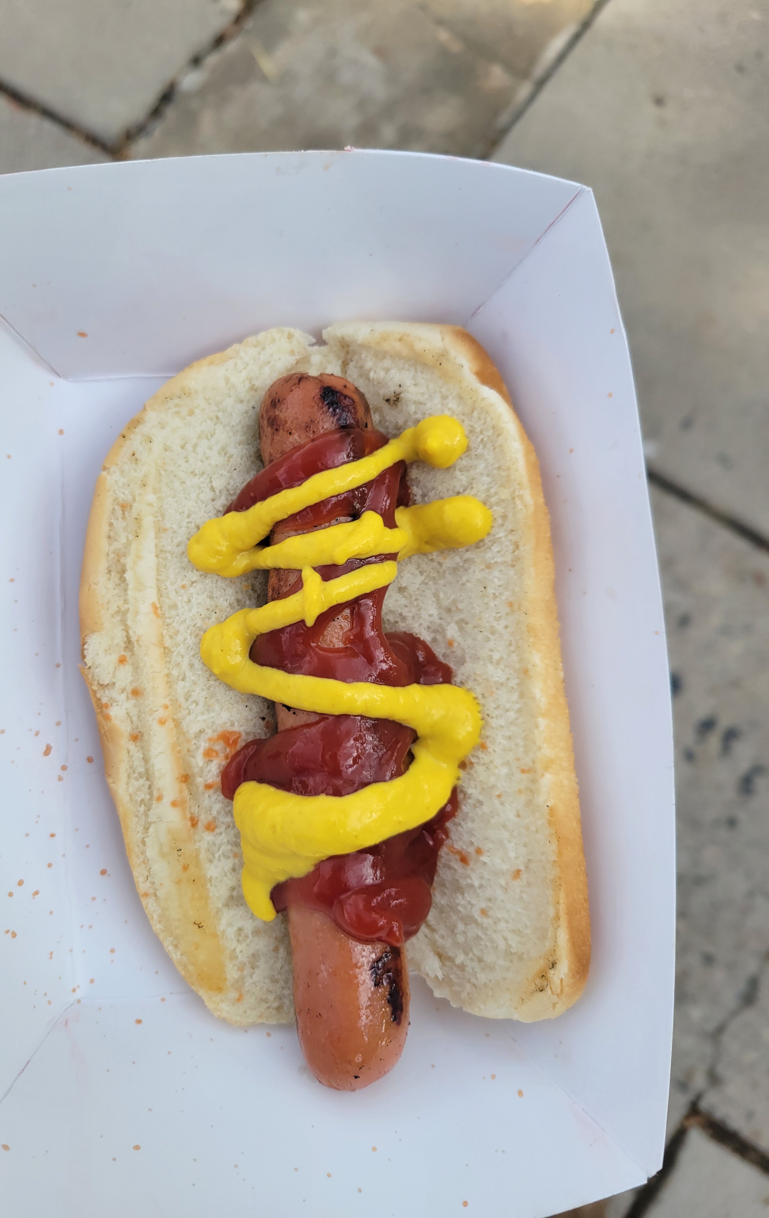Hot dog with mustard and ketchup on a bun that is on a paper tray.